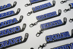 Multiple hockey stick keychains with player names and numbers printed on them in 3 layers with the base in black, the middle layer is white and the name and number is in blue