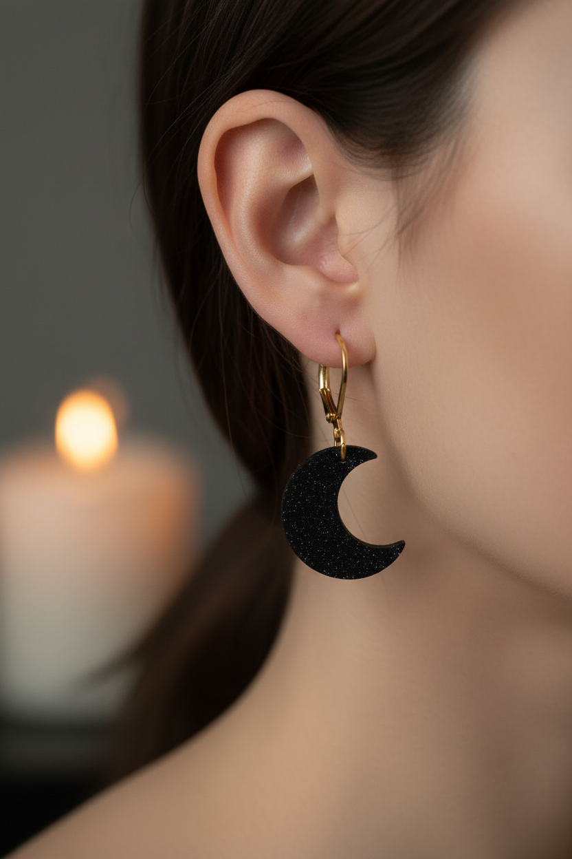 Black crescent moon earring worn by a person with a blurred candle in the background