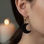 Black crescent moon earring worn by a person with a blurred candle in the background