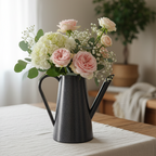 Black watering can with flowers on a tablecloth-covered table by Aurelis Design Studio
