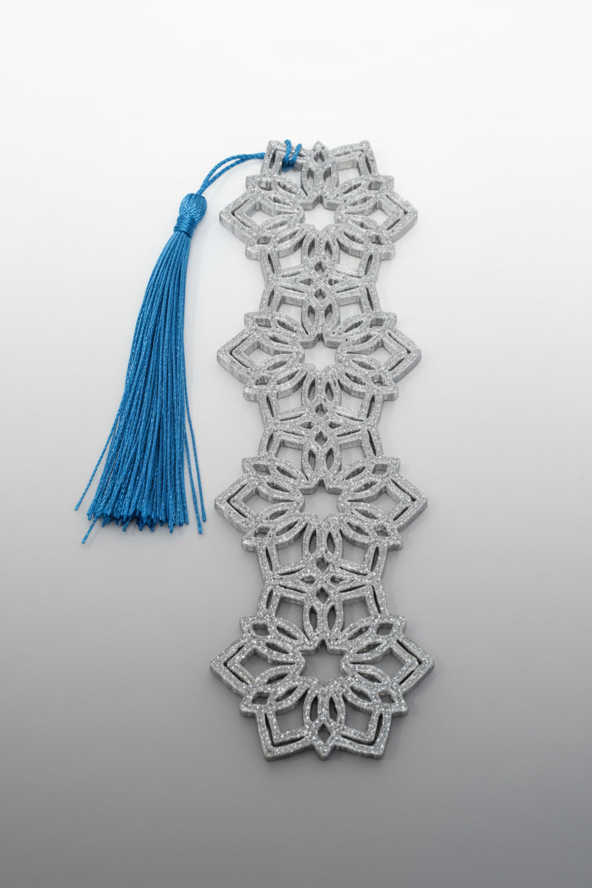 Decorative lace bookmark with snowflake patterns and a blue tassel on a light gray background