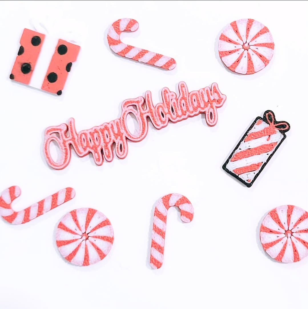 Custom 3D printed pieces by Aurelis Design Studio of Christmas elements including candy canes, peppermints, and a 'Happy Holidays' sign on a white background.