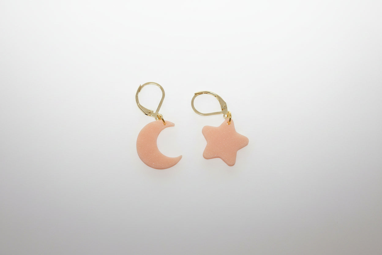 Pair of  peach earrings with moon and star shapes on a white background