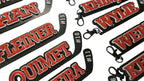 Multiple hockey stick keychains with player names and numbers printed on them in 3 layers with the base in black, the middle layer is white and the name and number is in red